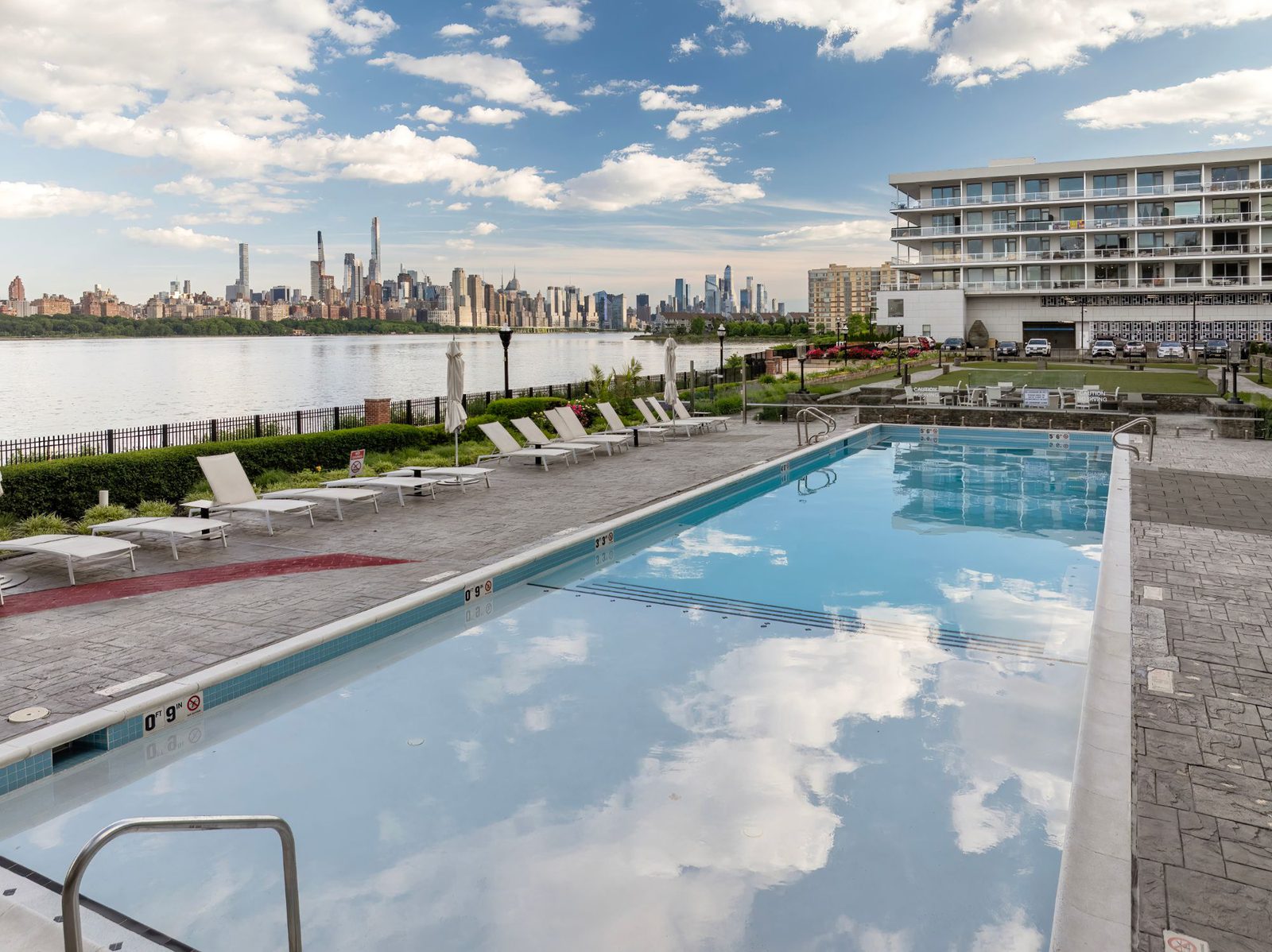 Waterfront pool and lounge chairs beside the Hudson River, with the Manhattan skyline across the water
